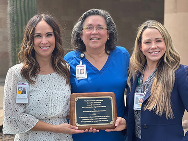 Ashlie Adams, Cheryl Scott, Tiffany Clark, standing outdoors with a plaque, representing the leadership at HonorHealth Rehab.