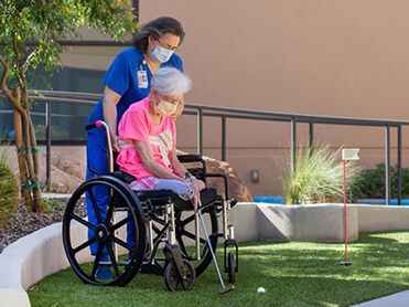 Older female limb loss survivor playing mini golf from her wheelchair.