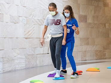 Female therapists helping male patient walk across colored discs to improve coordination.