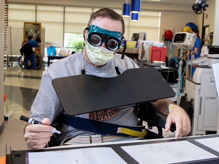 Young adult male wearing green safety goggles and doing draing therapy.