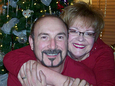 Dennis and Marsha in matching red sweaters in front of a Christmas tree.