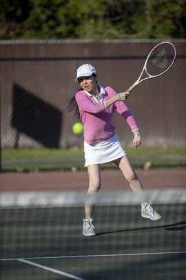 Female tennis player in pink jersey making a back swing on the court.