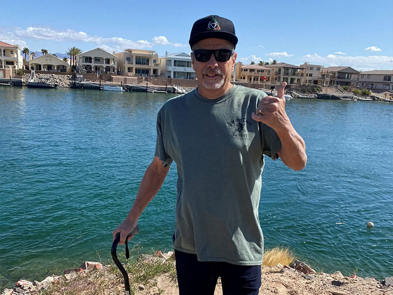 William, wearing sunglasses and black hat standing in front of body of water.